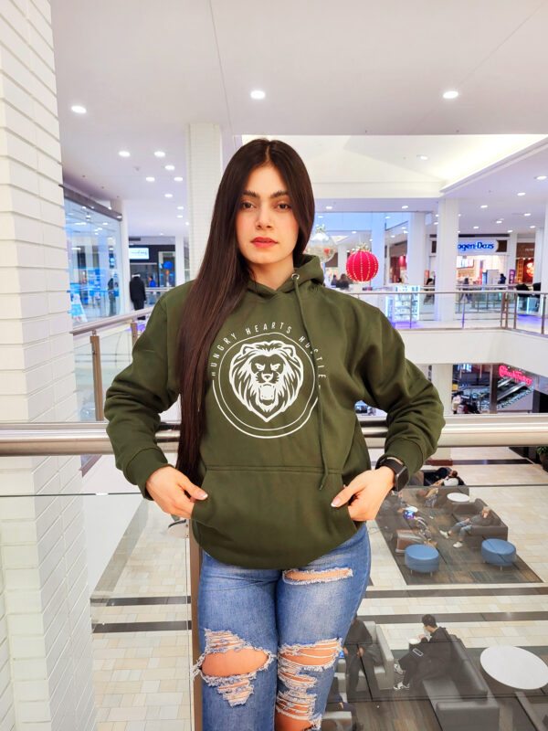 A woman standing in front of a store wearing jeans and a green hoodie.